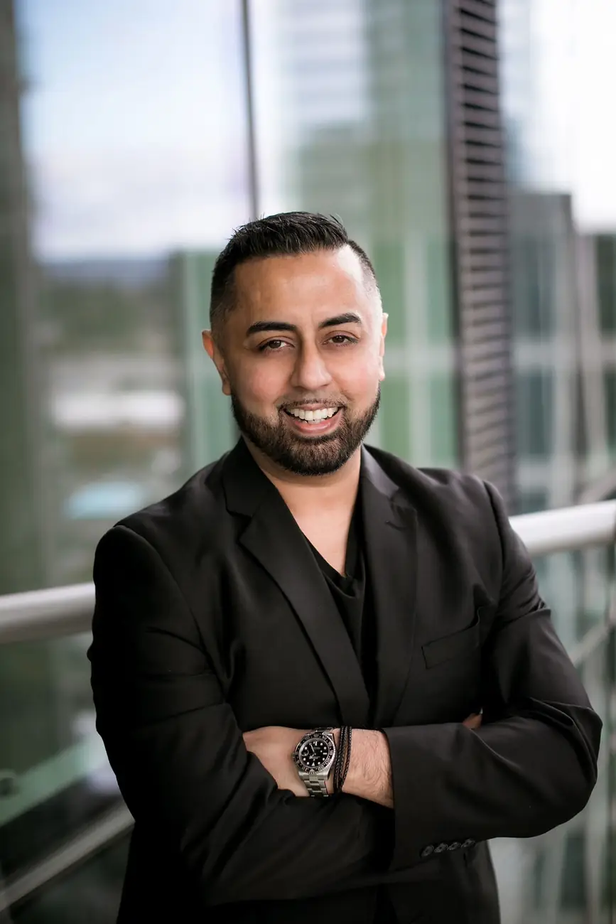 Omer Qureshi on a balcony with arms crossed and city behind.